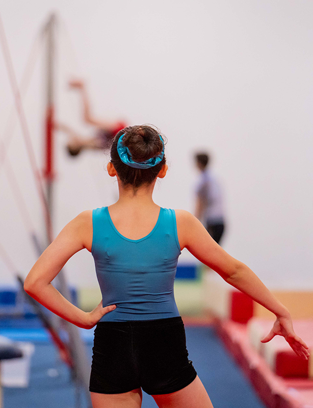 Female gymnast with blue leotard with her back to the camera doing a floor routine with her arm outstretched